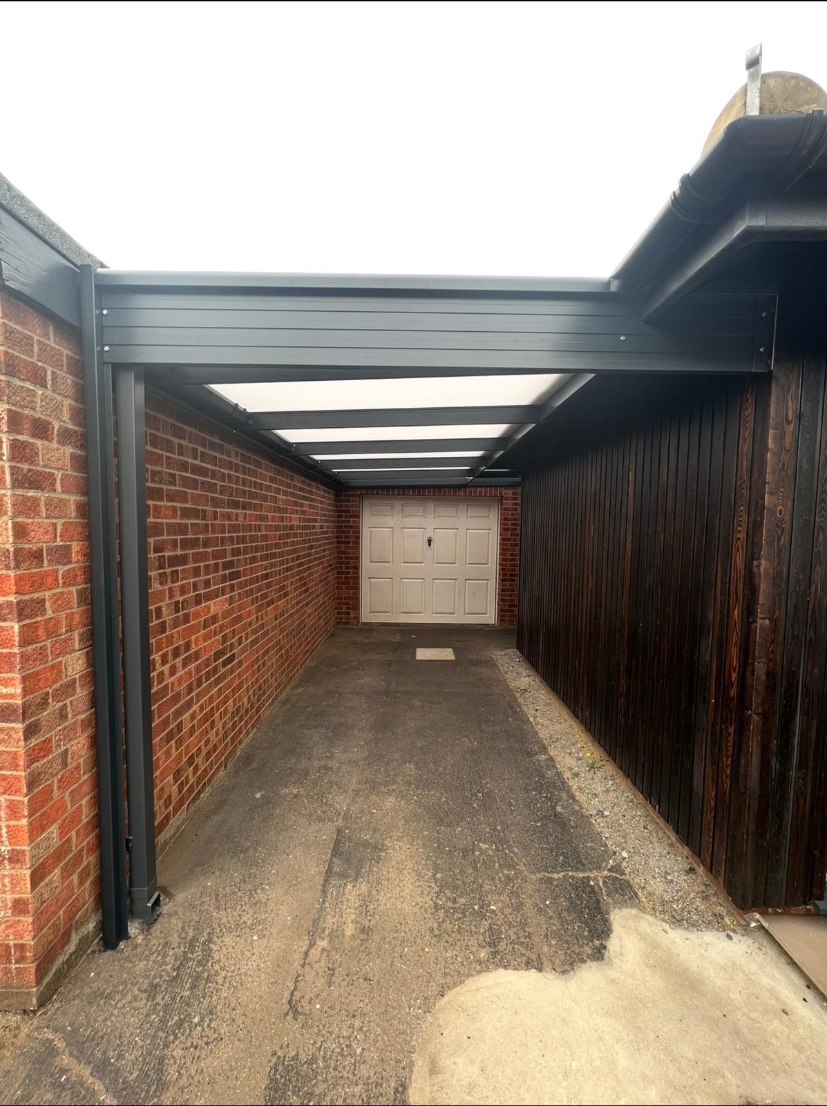 Long covered driveway canopy between a brick wall and timber boundary